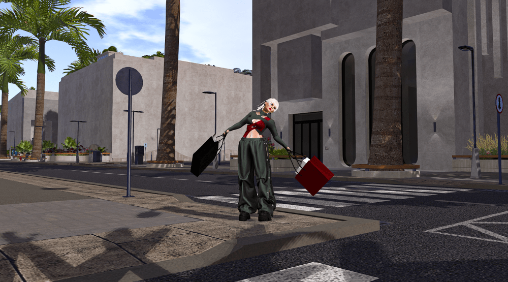 An avatar with short white hair stands on a street corner in a modern, concrete commercial district in Second Life, holding large black and red shopping bags in each hand. The avatar wears loose dark green pants and a cropped top, posing playfully as if showing off a successful shopping trip. Tall palm trees, minimalistic buildings, crosswalks, and street signs surround the scene, giving it a clean, urban look.